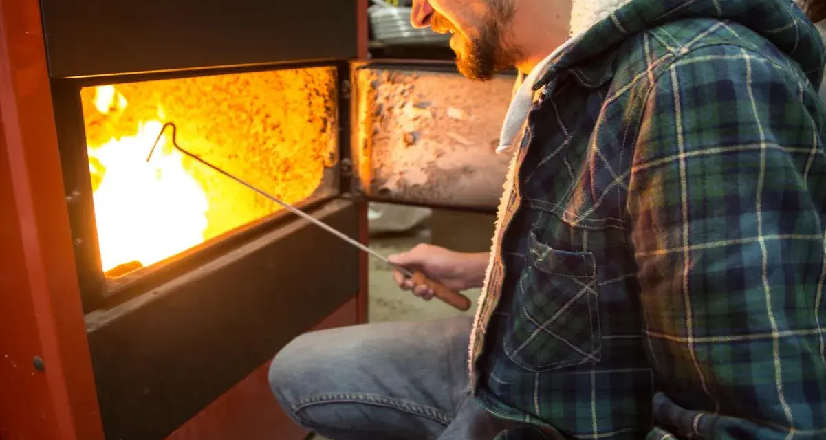 Uomo con camicia a quadri verde accende un fuoco in uno scaldabagno a legna, mostrando come funziona.