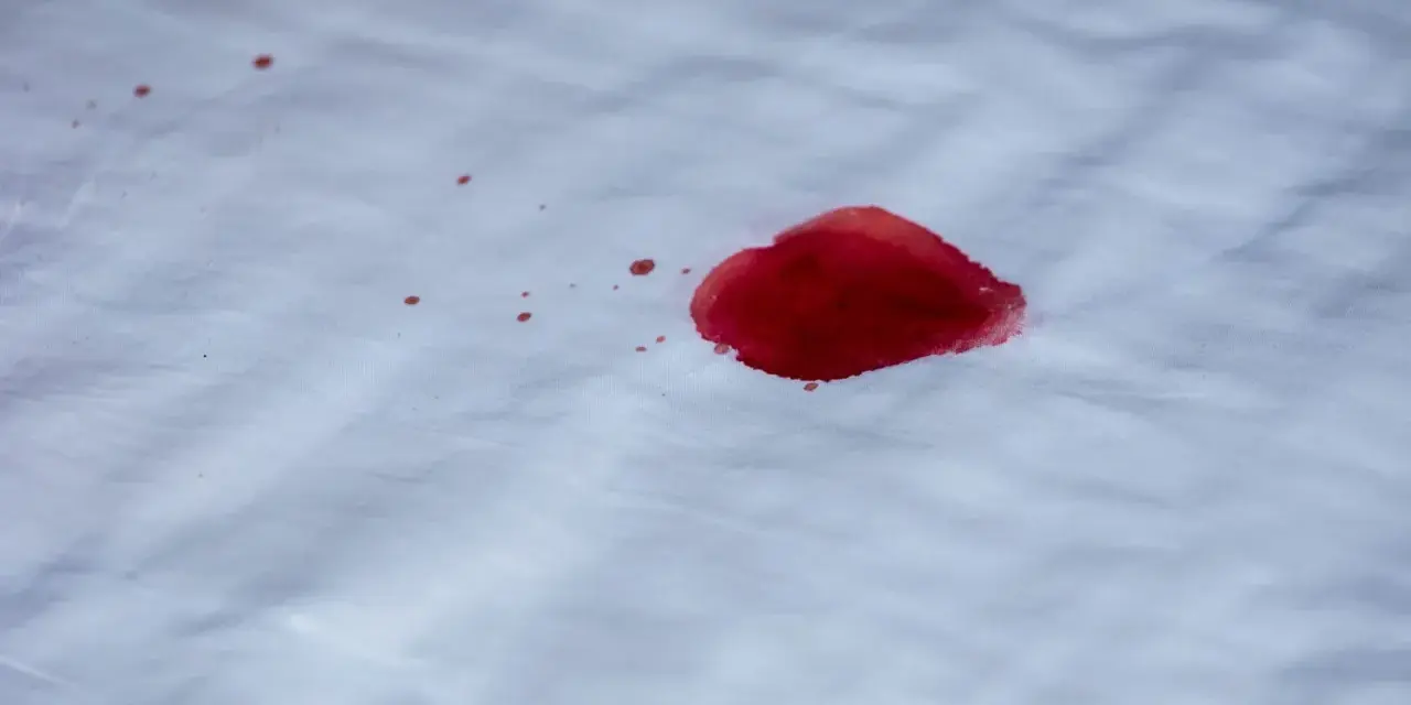 Une tache de sang rouge vif sur un tissu blanc. L'eau oxygénée pourrait aider à nettoyer cette tache.