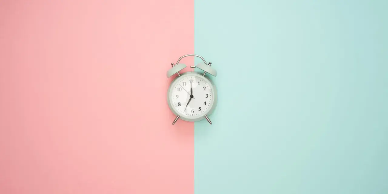 Wecker auf rosa und blauem Hintergrund. Zeit für Stundenreduzierung Schwangerschaft Gehalt.