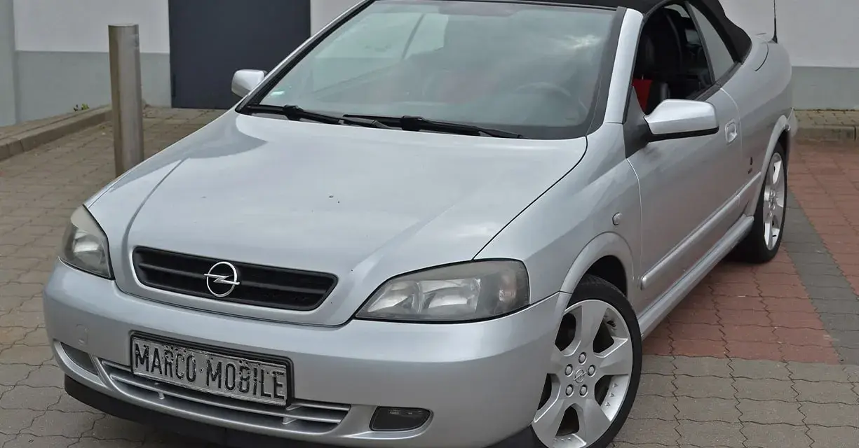 Silberner Opel Astra Bertone Cabrio mit offenem Verdeck, bereit für eine Spritztour.