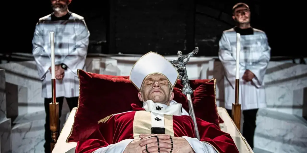 Papież w stroju, z różańcem, leży w trumnie. Obok stoją dwaj mężczyźni w białych szatach. Czy to bluźnierstwo, co to?