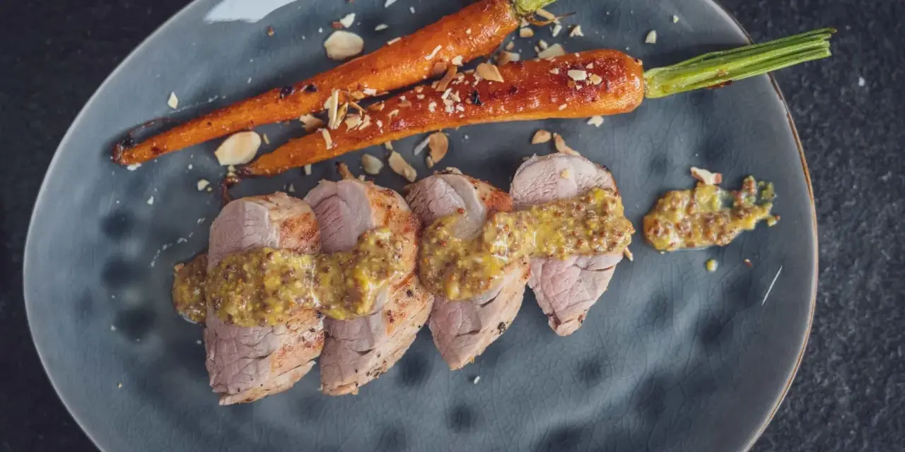 Perfekt gebratenes Schweinefilet mit Honig-Senf-Sauce und karamellisierten Karotten, bestreut mit Mandelsplittern.