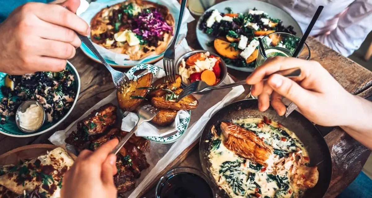 Leckeres Essen in einem Restaurant in Berlin Mitte: Pizza, Lachs, Rippchen und Salate werden von mehreren Händen geteilt.