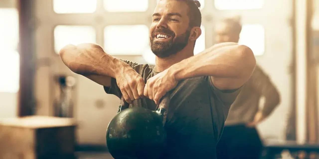 Un homme souriant effectue un exercice kettlebell, concentré sur son entraînement.