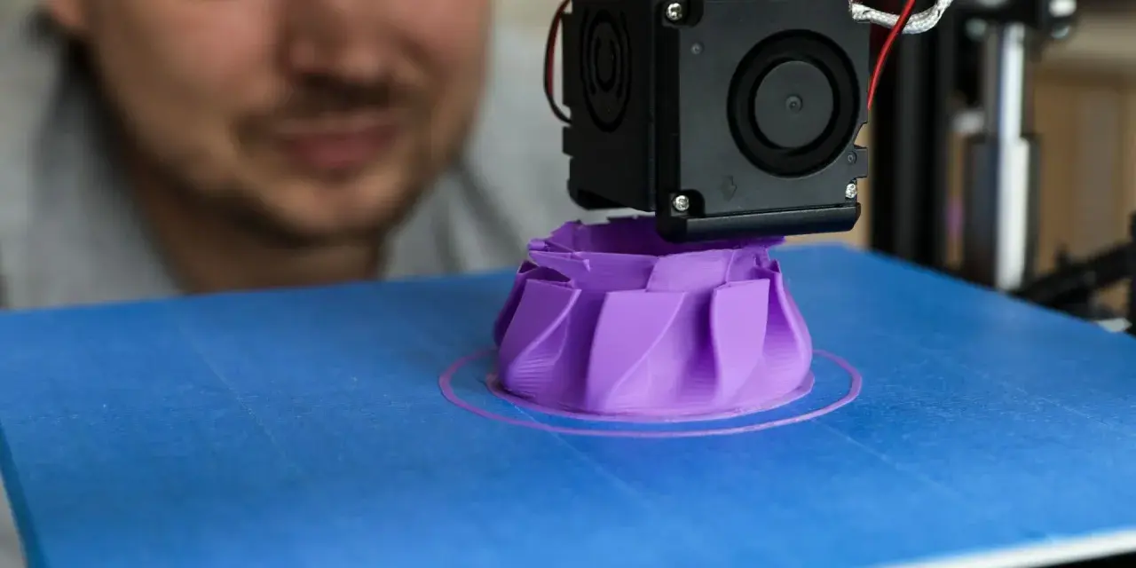A man watches his 3D printer create a purple object, showcasing its precise 3D printer specifications in action.