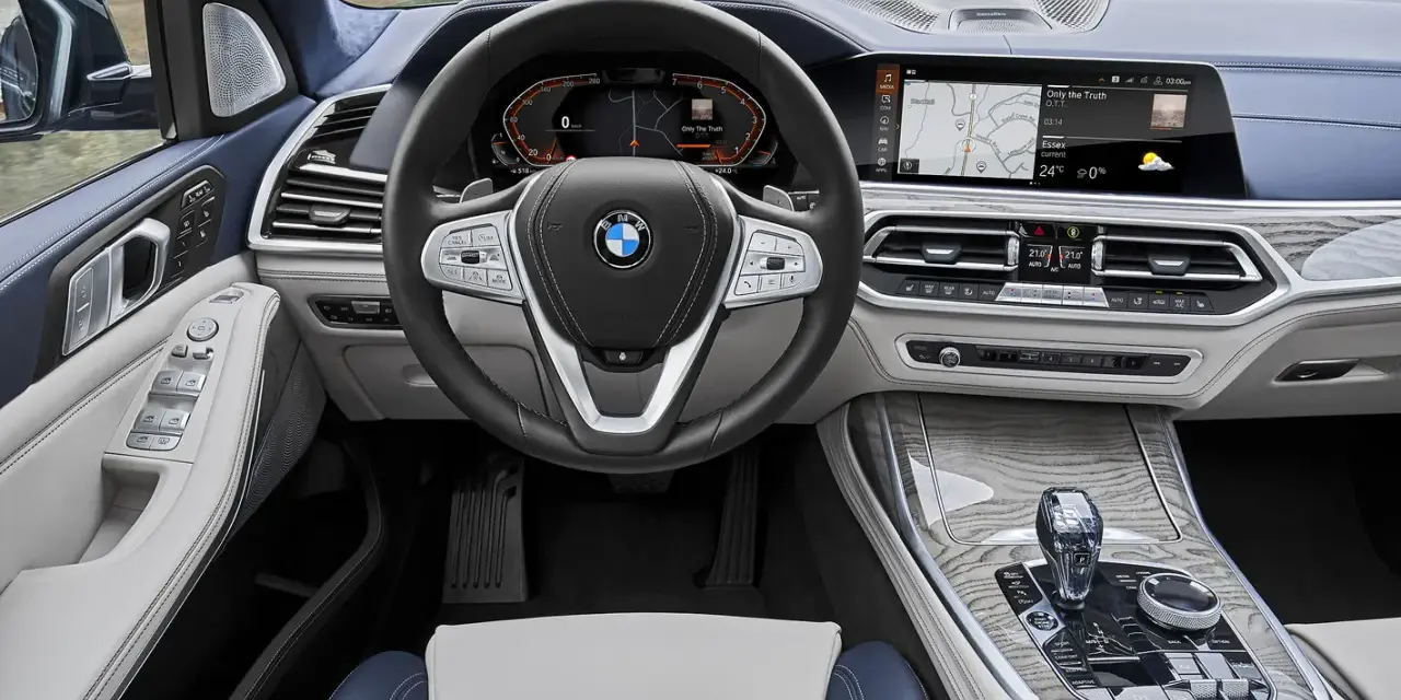 Wnętrze BMW X7: kierownica, ekran multimedialny z nawigacją i muzyką, panel klimatyzacji, dźwignia zmiany biegów.