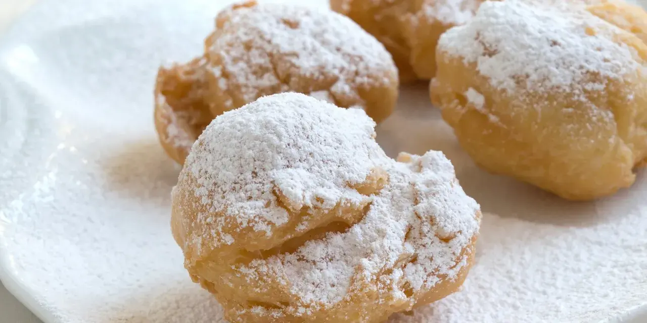 Vier goldbraune rheinische Krapfen, bestäubt mit Puderzucker, liegen auf einem weißen Teller.