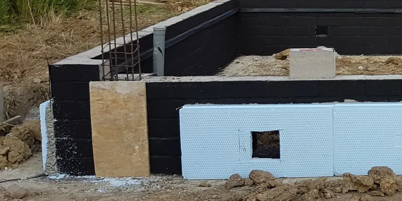 Fundament z czarną izolacją przeciwwilgociową i płytami XPS. Widać zbrojenie i fragmenty szalunku. Dobra jaka izolacja na fundament.