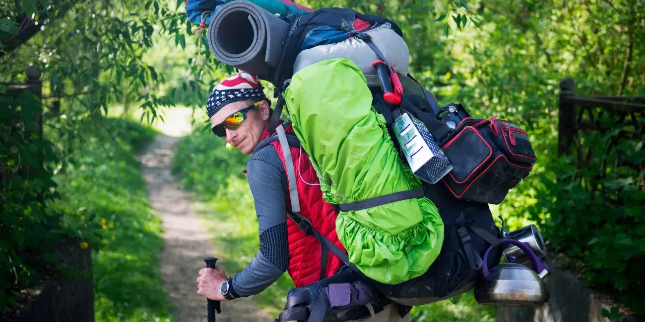 Un randonneur, prêt pour l'aventure, montre comment porter un sac à dos bien chargé avec une couverture de sol et une bouilloire.