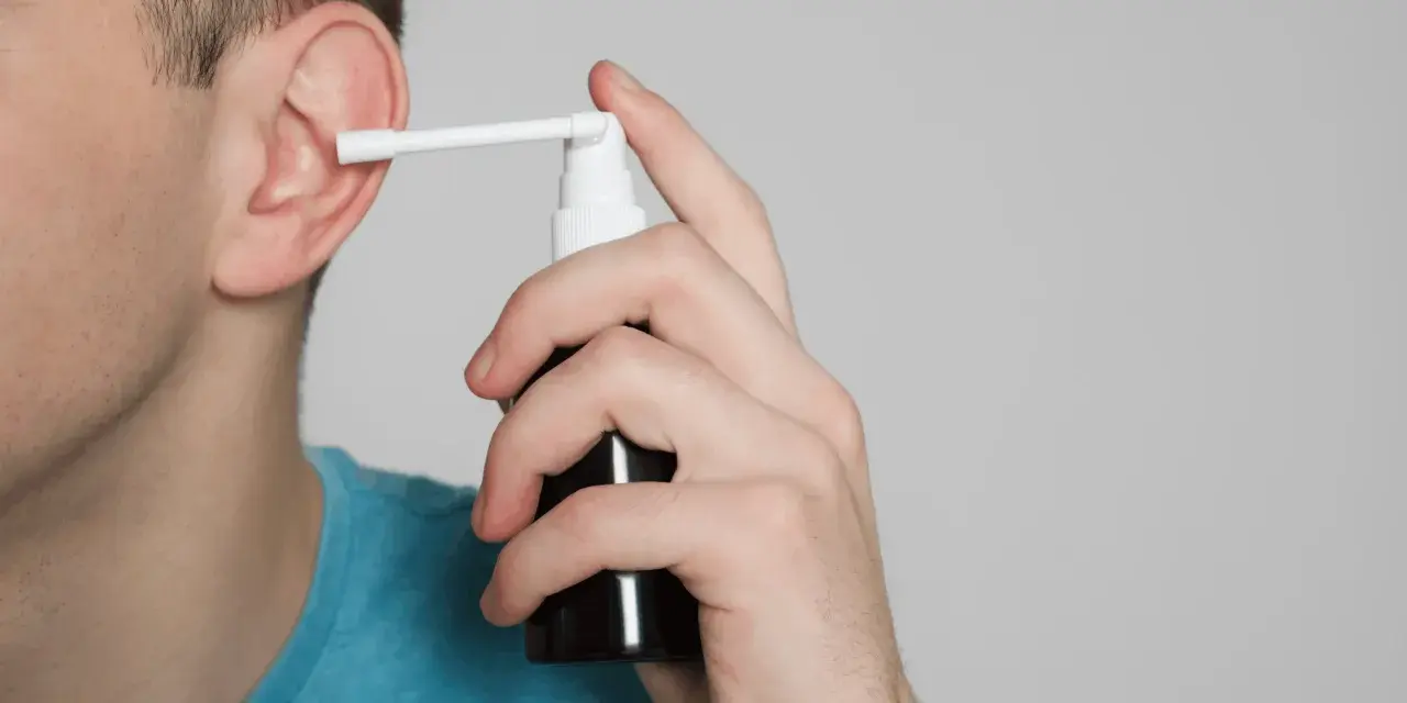 Mężczyzna aplikuje spray do ucha, łagodząc płyn w komórkach wyrostka sutkowatego.