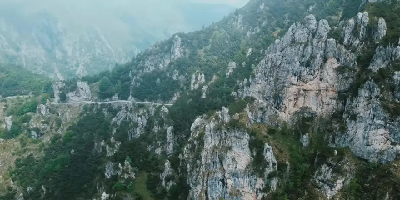 Strada tortuosa che sale verso il passo Barmone, tra rocce imponenti e vegetazione lussureggiante.