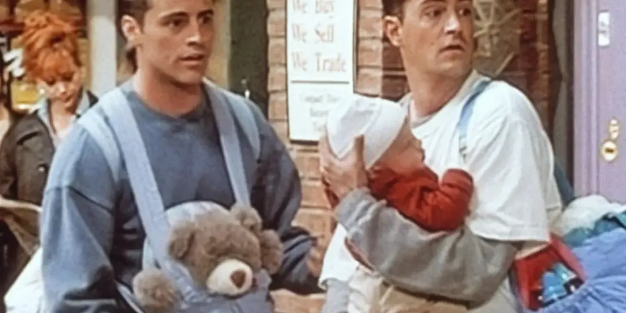 Chandler i Joey z dzieckiem i misiem w nosidełku. Chandler wygląda na lekko zaniepokojonego.