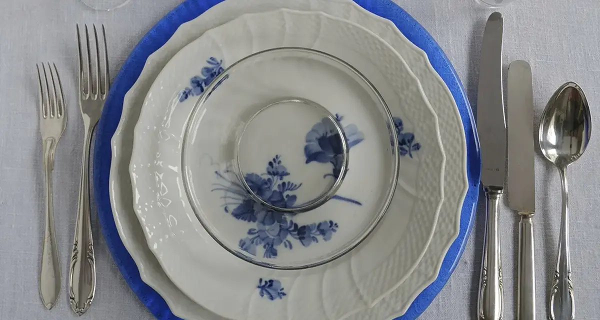 Vacker dukning med blå och vit porslin, bestick och glas. En elegant dessert tallrik väntar på att fyllas.