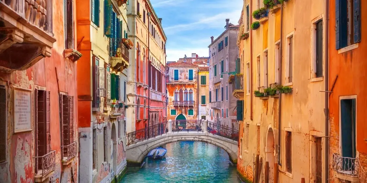 Canale veneziano con palazzi colorati e un ponte. Si immagina come fu costruita Venezia, su palafitte e ingegno.