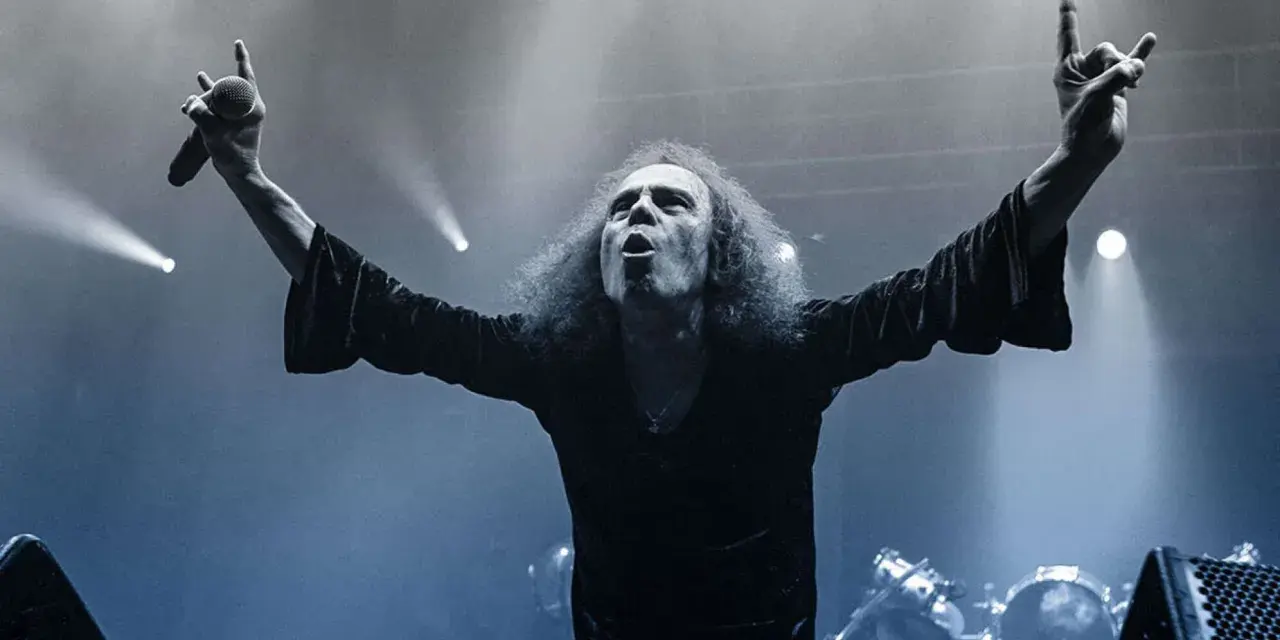 Ronnie Dio mit erhobenen Armen und Mikrofon, die Hand zum "Rock on"-Gruß geformt.