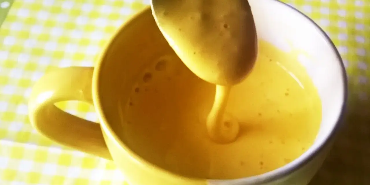 Kogel mogel przepis w filiżance, łyżka z gęstym, żółtym kremem spływa do naczynia.
