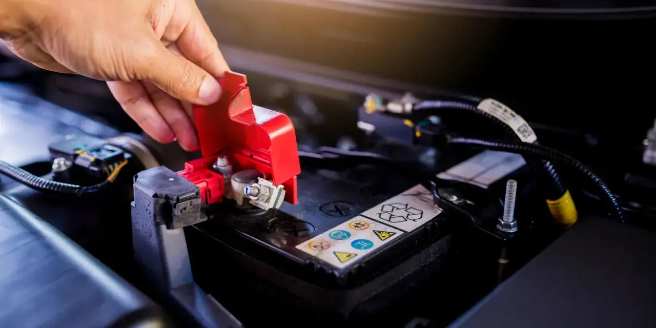 Mano che solleva il coperchio rosso di protezione del polo della batteria, un passo fondamentale per imparare come cambiare la batteria della macchina.