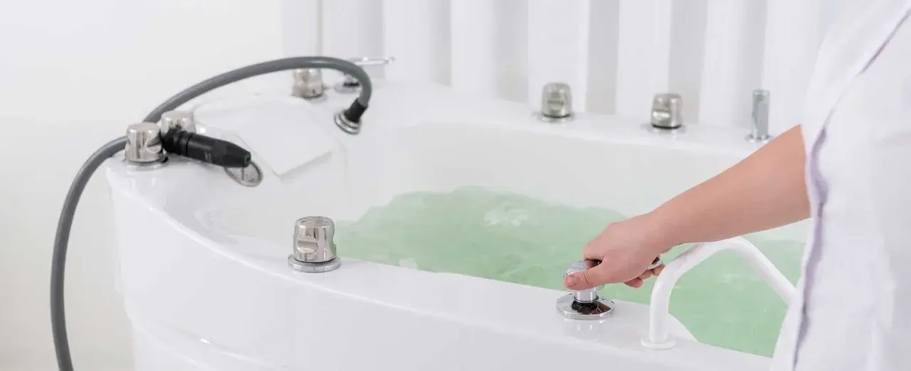 Dłoń reguluje strumień wody w wannie, przygotowując relaksujący masaż wirowy.