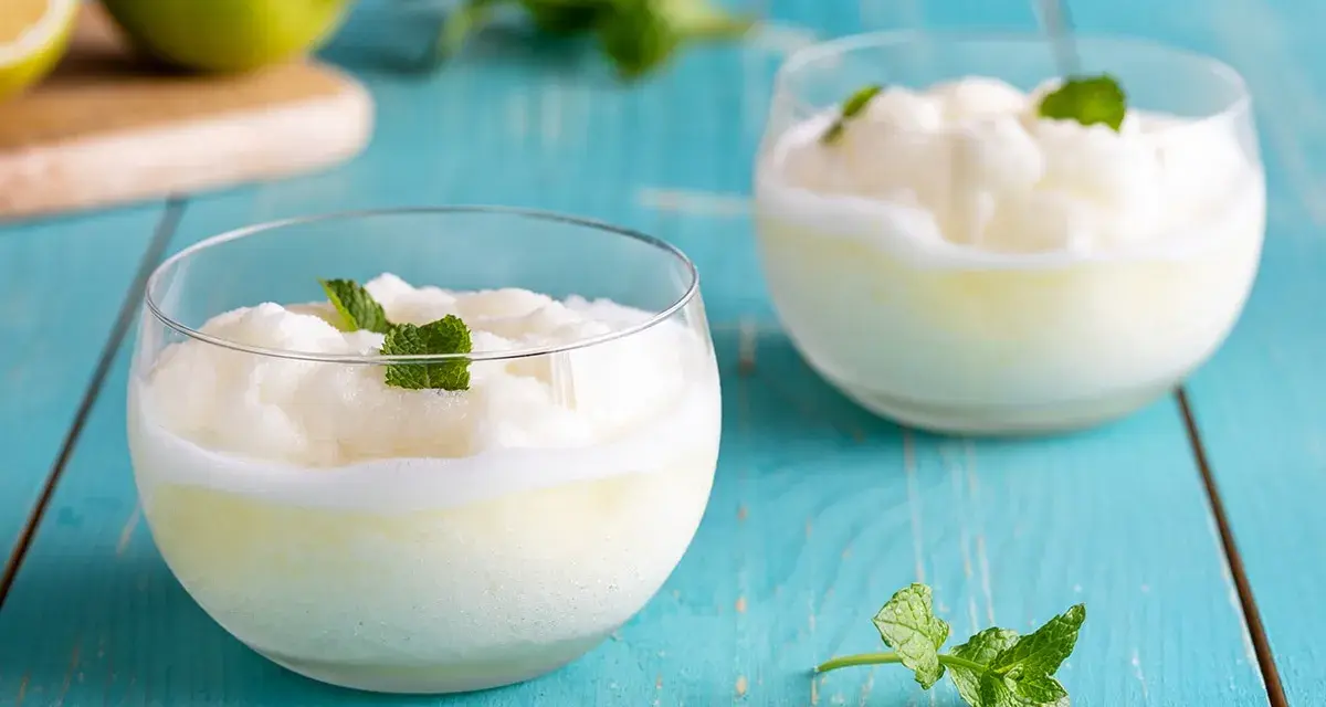 Due bicchieri di sorbetto al limone senza albume, guarniti con menta fresca, su un tavolo di legno blu.
