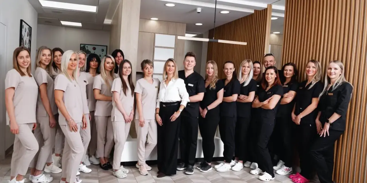 Grupa uśmiechniętych dentystów i personelu medycznego w jasnych i ciemnych uniformach stoi w nowoczesnym gabinecie.