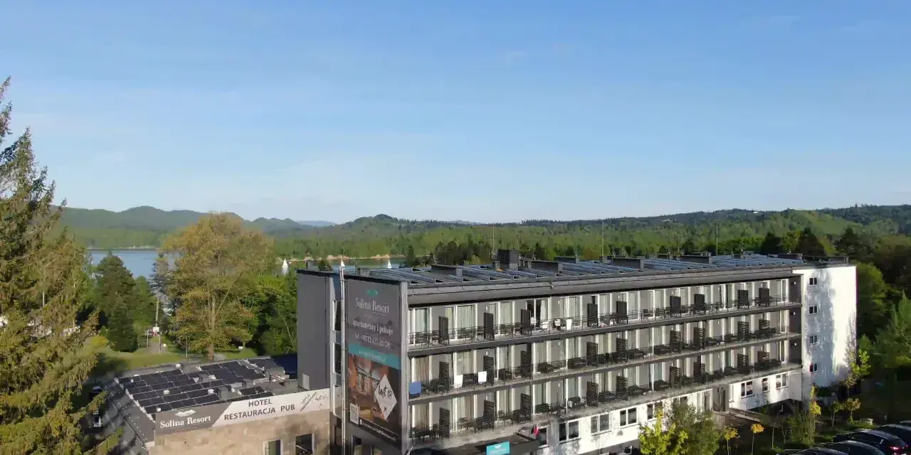 Widok na hotel Solina Resort & Spa z apartamentami i pokojami, otoczony zielenią, z jeziorem Solina w tle.