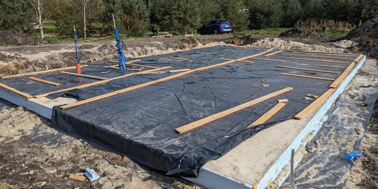 Płyta fundamentowa z folią i drewnianymi elementami na budowie domu szkieletowego.