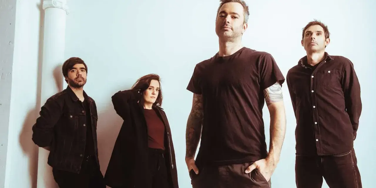 Quatre musiciens, un groupe rock canadien francophone, posent devant un mur blanc.