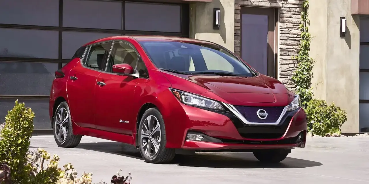 Czerwony Nissan Leaf przed nowoczesnym domem. Sprawdź atrakcyjną nissan leaf cena i wybierz swój wymarzony samochód elektryczny.