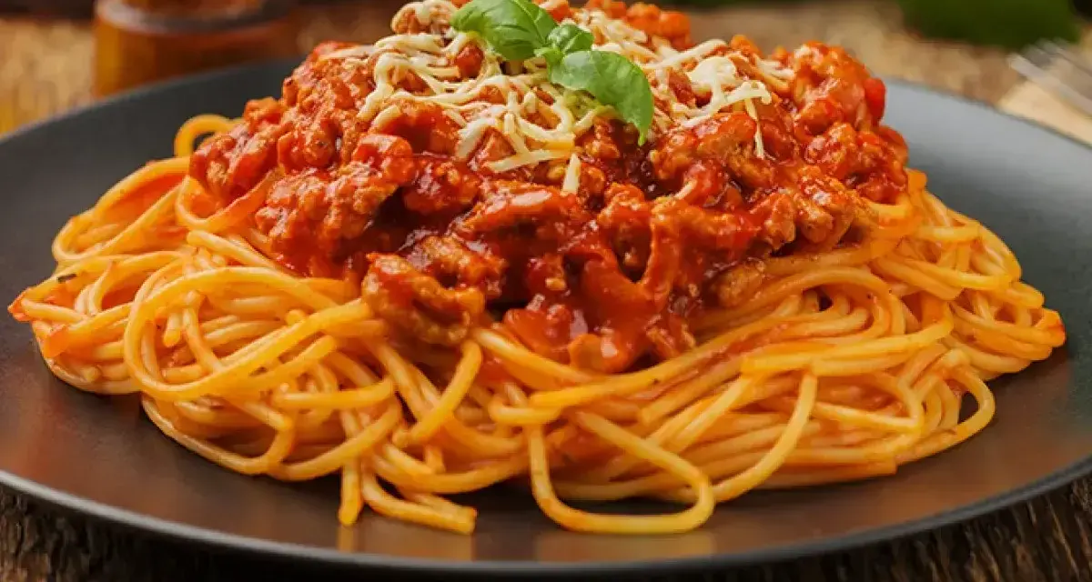 Talerz pełen najsmaczniejszego spaghetti bolognese, udekorowany listkiem bazylii i startym serem.