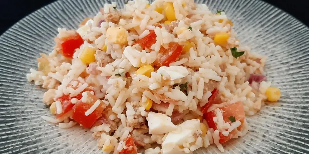 Une généreuse portion de salade de riz thon, garnie de dés de tomates, de maïs et d'œufs durs, sur une assiette texturée.