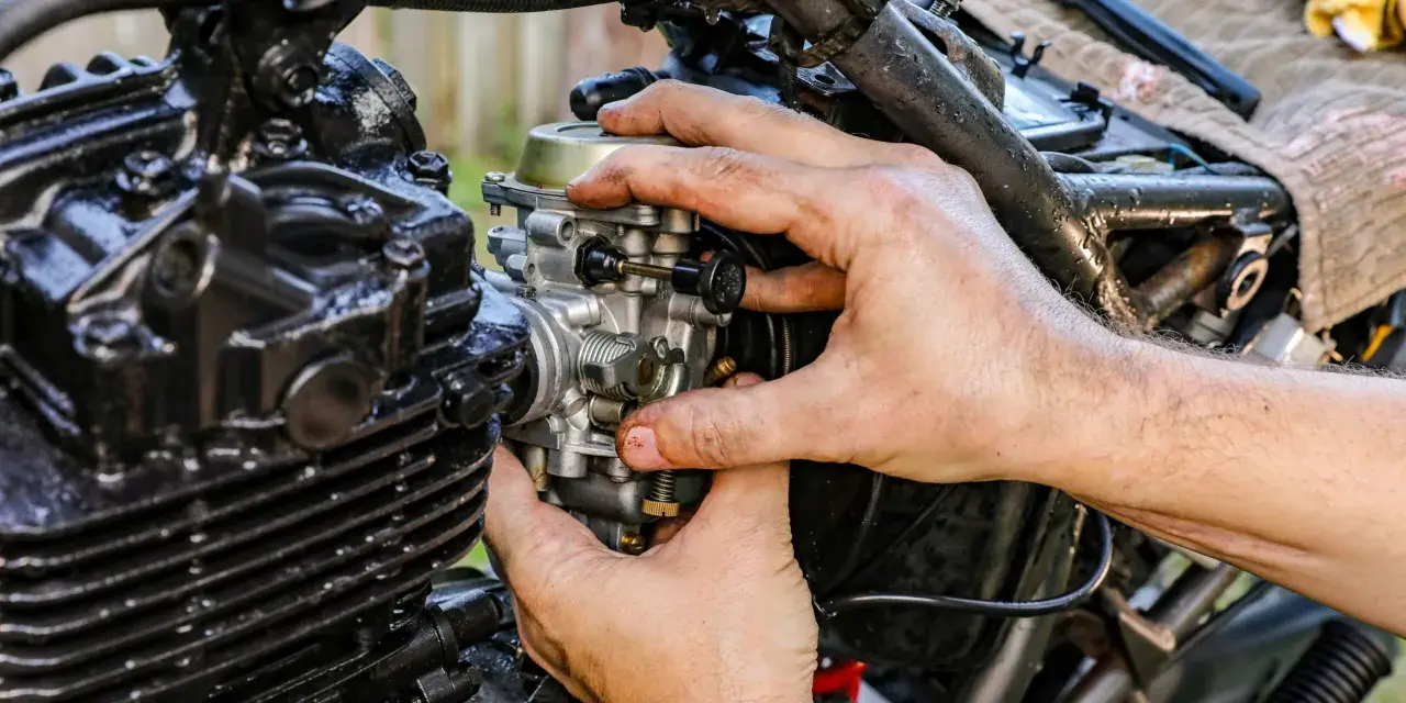 Ręce mechanika regulują gaźnik motocykla, pokazując, jak działa ssanie.
