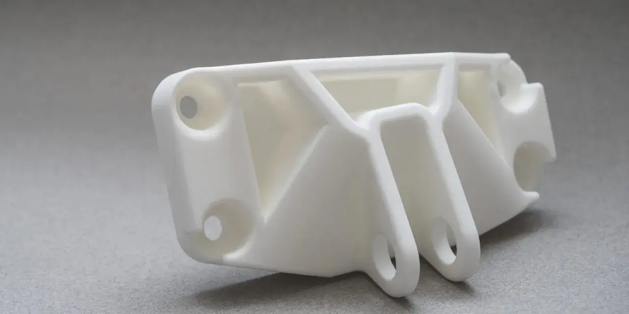 A white, complex SLS part with multiple holes and support structures, ready for assembly.