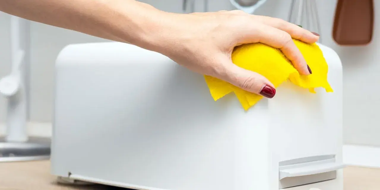 Eine Hand wischt mit einem gelben Tuch über einen weißen Toaster. So einfach ist das Toaster reinigen für ein blitzsauberes Ergebnis.