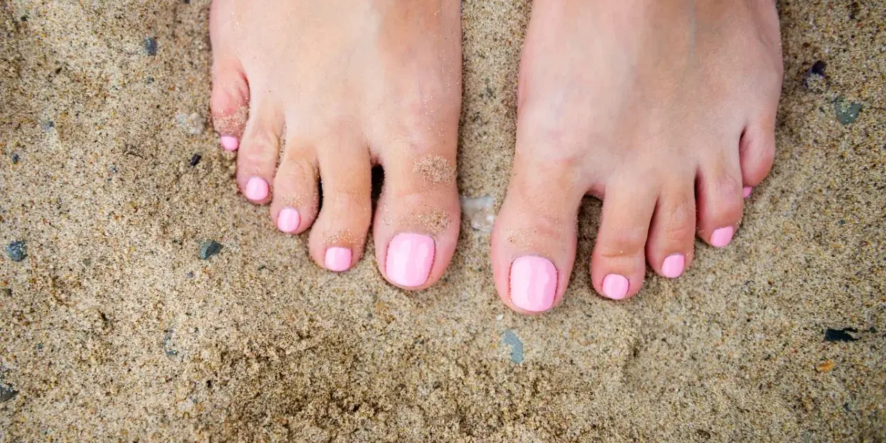 Stopy na piasku z różowym, modnym pedicure. Idealne na lato.