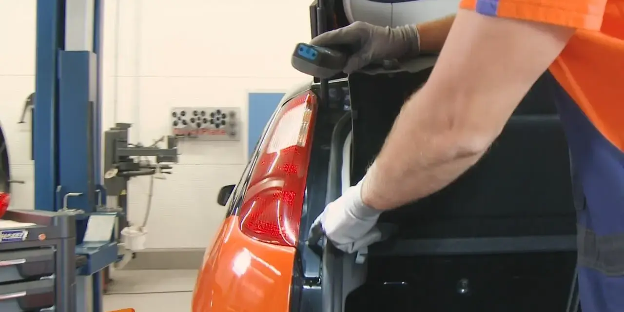 Ein Mechaniker wechselt das Bremslicht eines Ford Focus. Er hält ein Werkzeug in der Hand und arbeitet am Heck des Autos.
