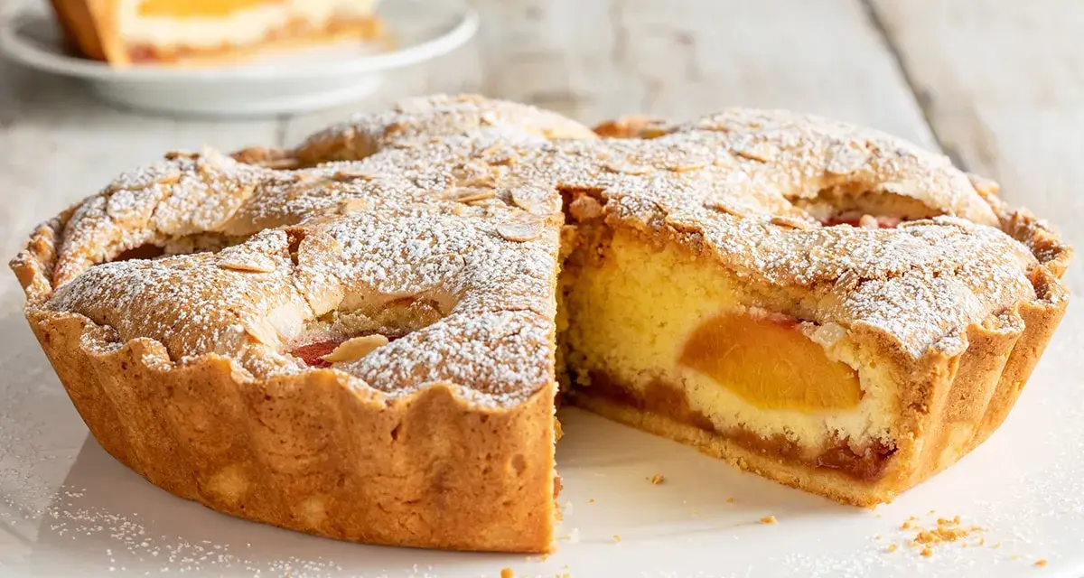 Una fetta di torta alle pesche, con la crosta dorata e un ripieno succoso, cosparsa di zucchero a velo e mandorle.