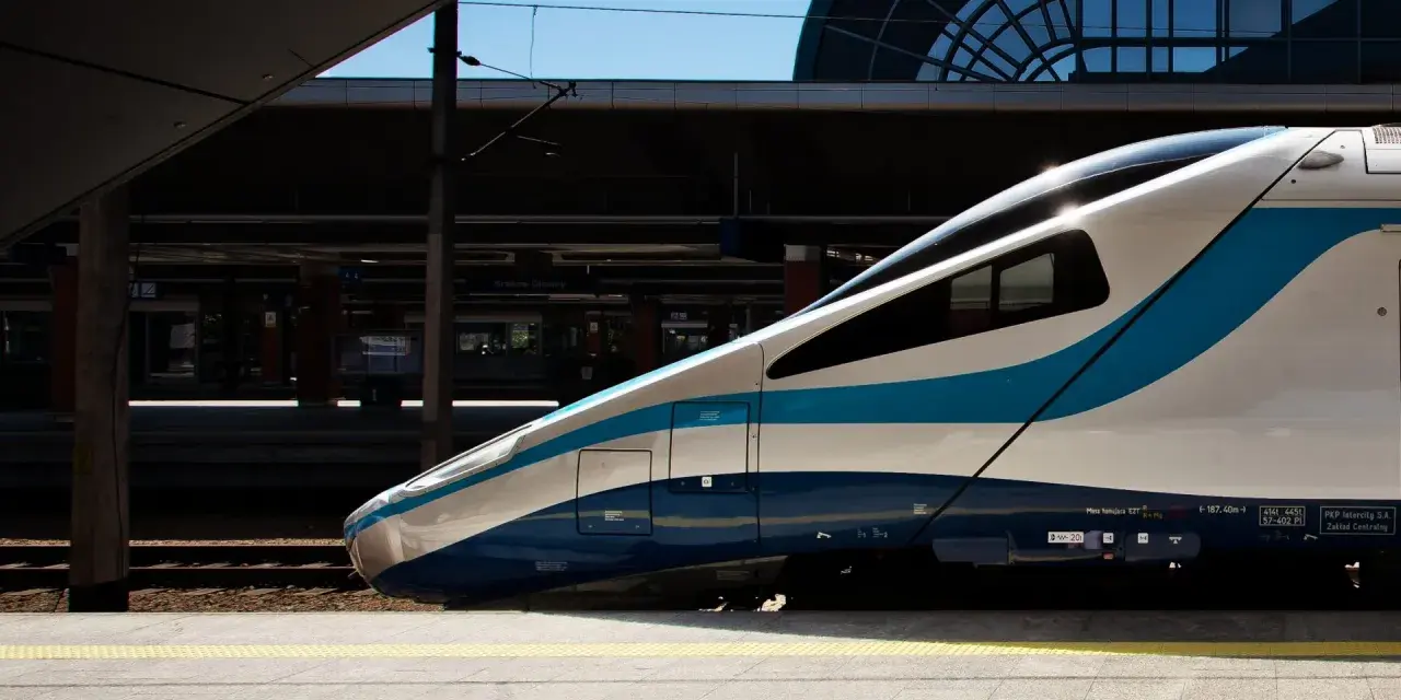 Nowoczesny pociąg PKP Intercity z niebieskimi pasami na tle dworca.