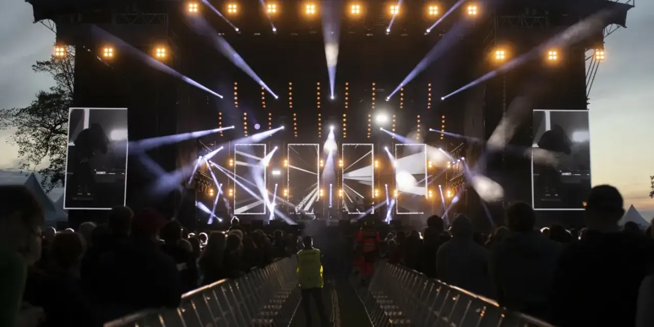 Jarocin Festiwal rozświetlony tysiącami świateł. Tłum czeka na koncert, a na scenie widać artystów.