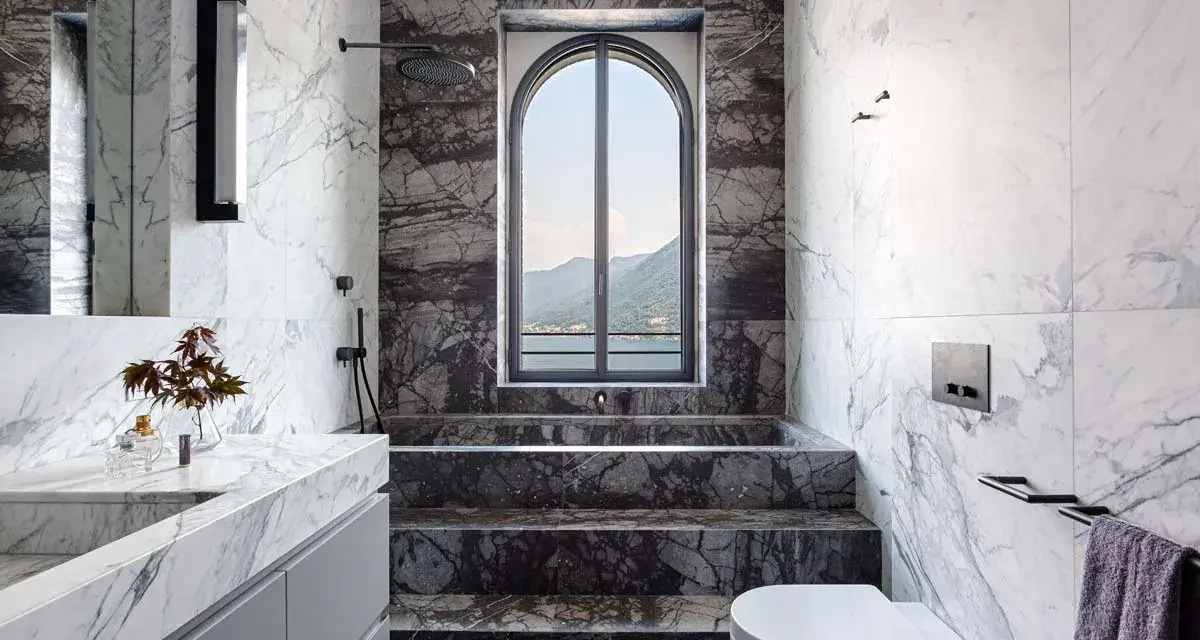 Bagno di lusso con vasca doccia in muratura, rivestimenti in marmo e vista panoramica.
