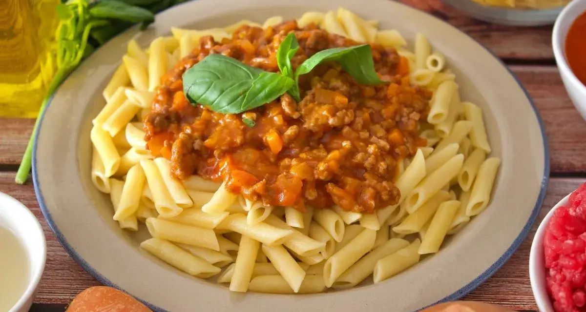 Plato de macarrones a la boloñesa, con salsa de carne y tomate, decorado con hojas de albahaca fresca.