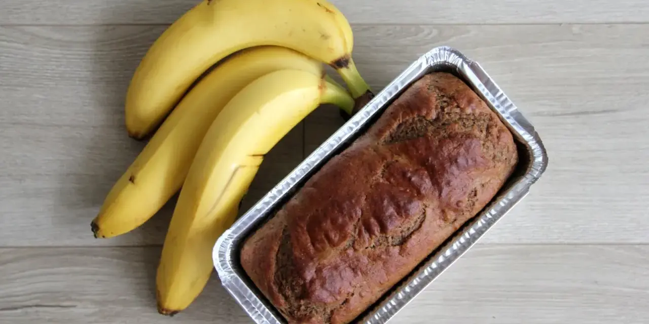 Gotowy proteinowy chlebek bananowy w formie, obok pęk dojrzałych bananów.