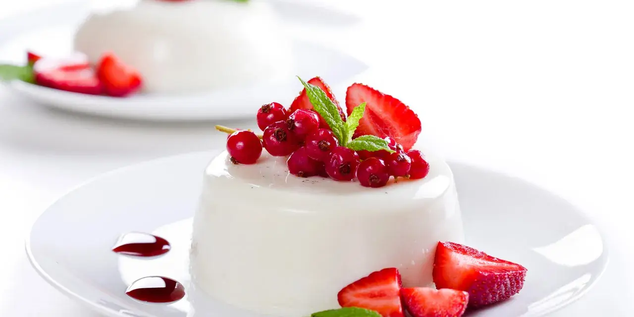 Deliciosa panna cotta cremosa adornada con fresas, grosellas rojas y menta fresca.