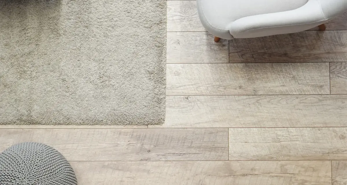 Elige el color del suelo de una casa con este suelo de madera clara, alfombra beige y puf gris.