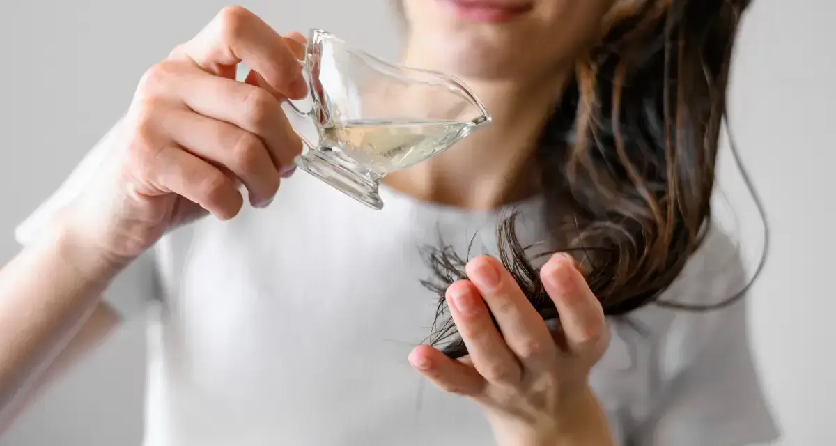 Kobieta aplikuje hydrolat do włosów, przelewając go z małego naczynia na pasma włosów.