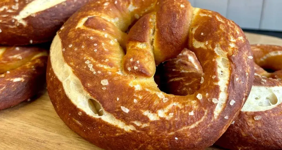 Frisch gebackene, goldbraune sauerteig brezeln mit grobem Salz bestreut, liegen auf einem Holzbrett.
