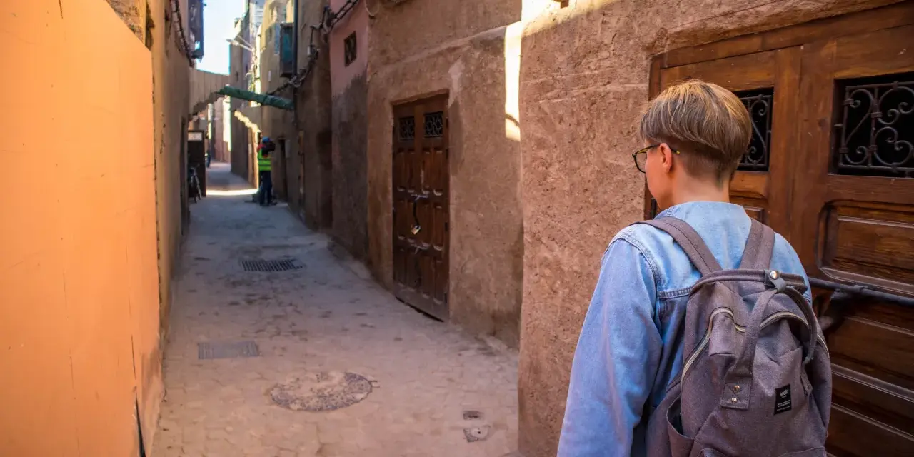 Młoda osoba z plecakiem idzie wąską uliczką w Marrakeszu. Czy w Marrakeszu jest bezpiecznie? Tak, zwiedzanie jest przyjemne.