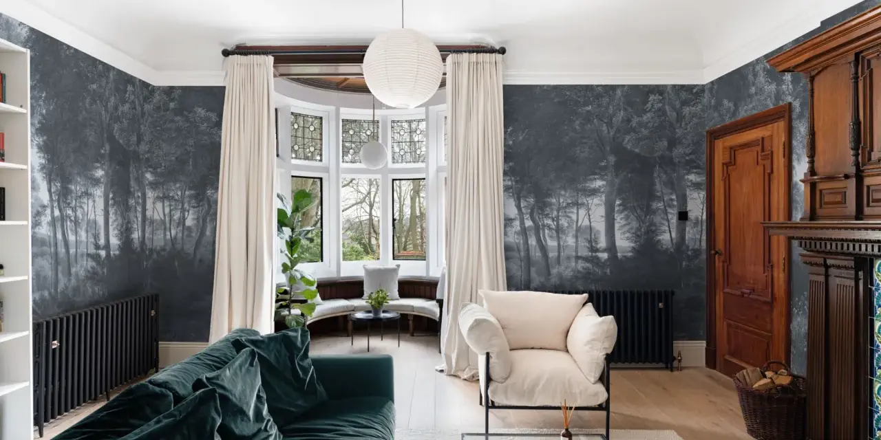 Sala con papel pintado de bosque, sofá verde, sillón beige y chimenea de madera. Ideas de como poner papel pintado para transformar tu hogar.