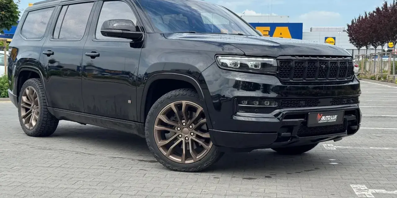 Czarny Grand Wagoneer z brązowymi felgami stoi na parkingu przed sklepami.