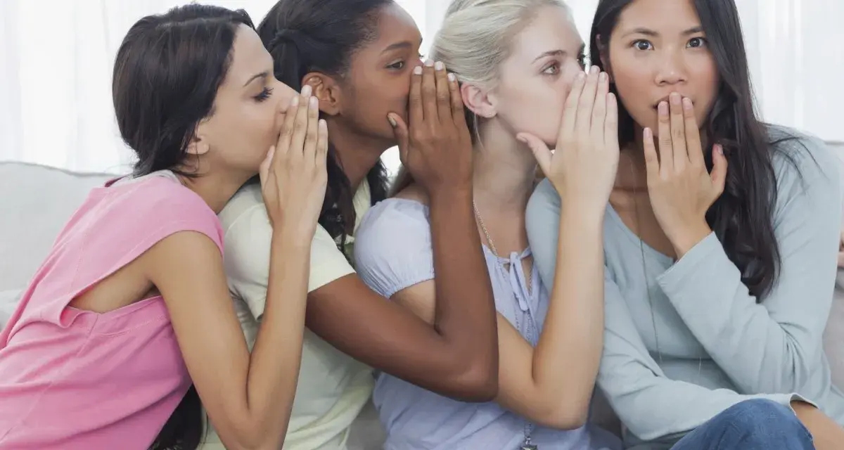 Four friends share secrets, whispering what is gossip. One girl looks surprised as the whispers continue.