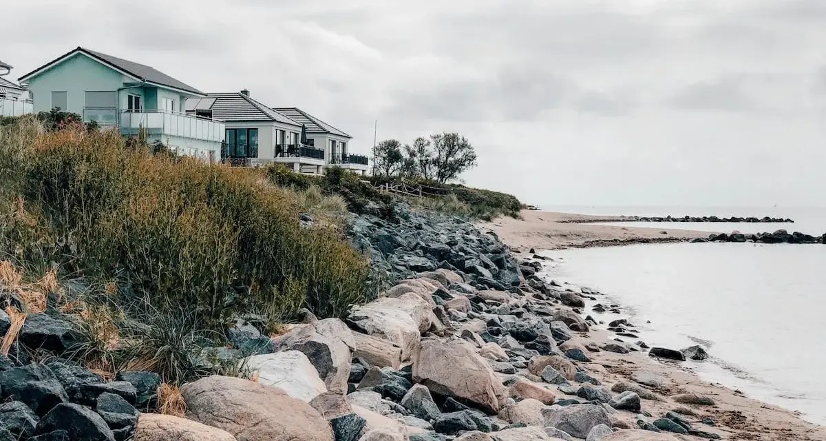 Häuser am Hang über einem steinigen Strand. Ein ruhiger Ort, der zu den Fehmarn Geheimtipps zählt.